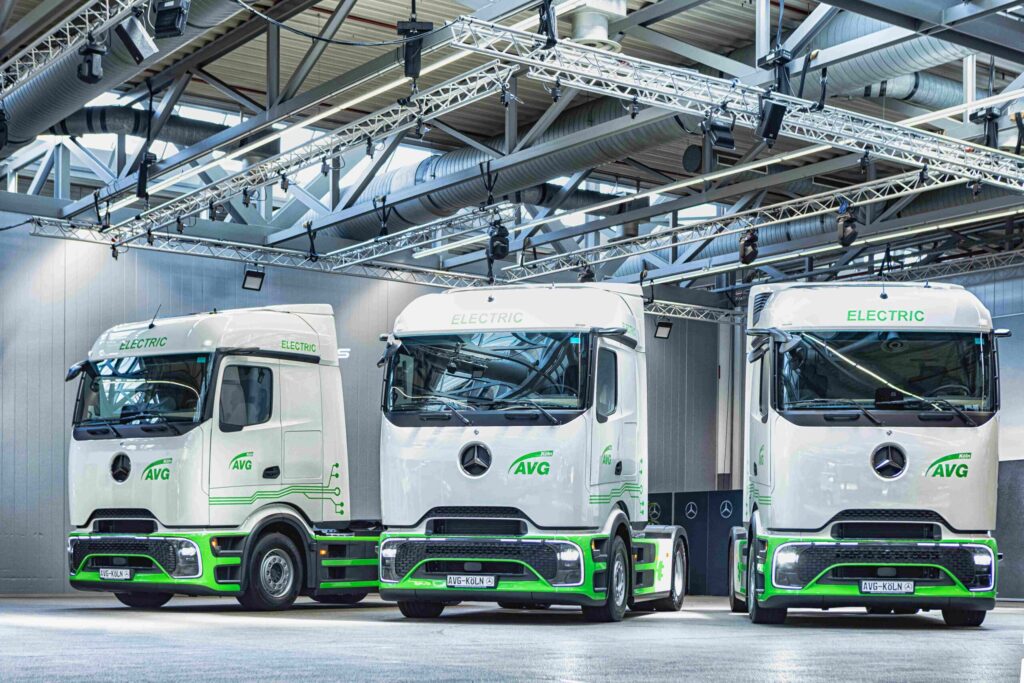 Drei mit den Logos der AVG Köln beschriftete Sattelzugmaschinen Mercedes-Benz eActros 400 nebeneinander in einer Halle