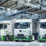 Drei mit den Logos der AVG Köln beschriftete Sattelzugmaschinen Mercedes-Benz eActros 400 nebeneinander in einer Halle