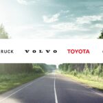 Eine Grafik, die die Schriftzüge von Daimler Truck, Volvo, Toyota und Cellcentric zeigt (v.l.n.r.), im Hintergrund eine Landstraße durch einen Wald