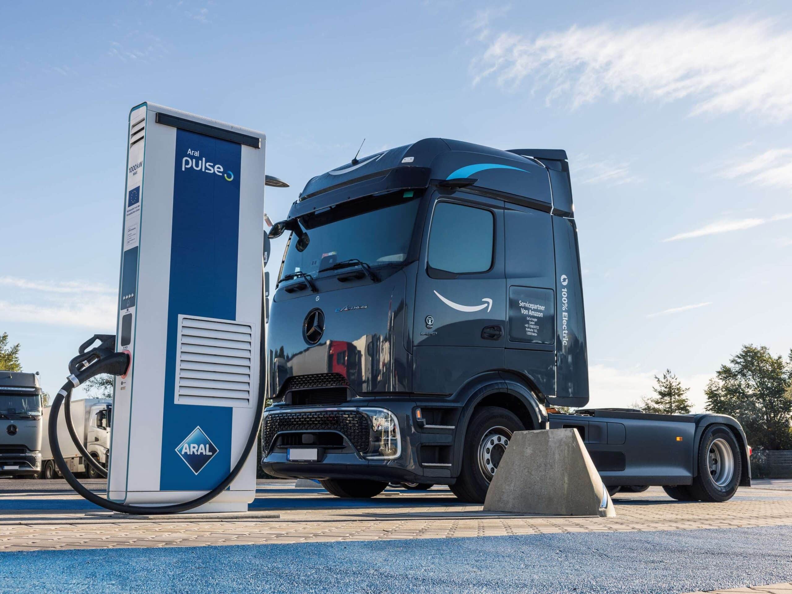Eine batterieelektrische Sattelzugmaschine vom Typ Mercedes-Benz eActros 600 mit Aufschrift „Servicepartner von Amazon“ an der Seite steht an einer Megawatt-Ladesäule von Aral pulse