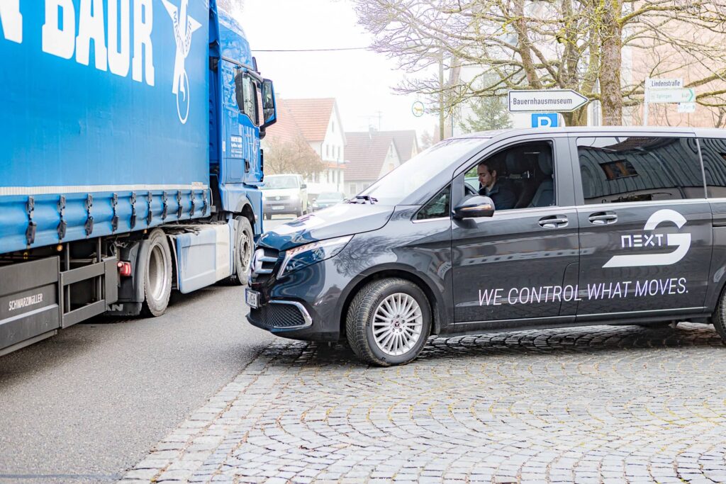 Eine ferngesteuerte Mercedes-Benz V-Klasse hält an einer Kreuzung, über die gerade ein Lkw fährt