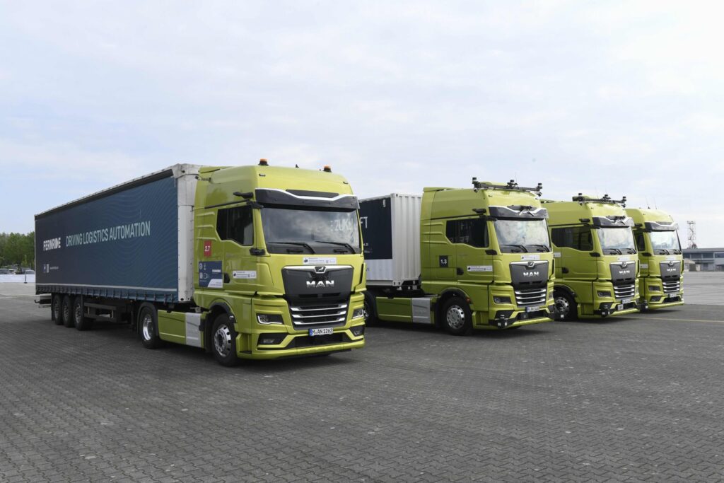 Vier Prototypen autonom fahrender Sattelzüge auf Basis MAN nebeneinander auf einem Parkplatz