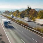 Blick auf eine bundesdeutsche Autobahn mit fließendem Verkehr von schräg oben, wobei in der Langzeitbelichtung die Fahrzeuge nur schemenhaft zu erkennen sind
