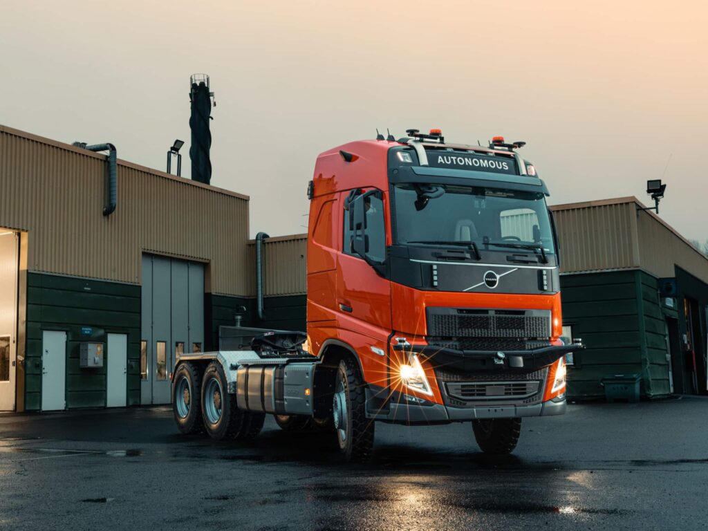 Eine autonom fahrende Dreiachs-Sattelzugmaschine auf Volvo-Basis, abgesattelt bei Dämmerung vor einer Halle
