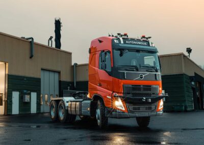 Eine autonom fahrende Dreiachs-Sattelzugmaschine auf Volvo-Basis, abgesattelt bei Dämmerung vor einer Halle