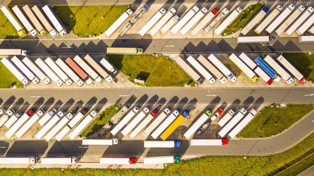 Ein stark belegter Lkw-Parkplatz aus der Vogelperspektive; man sieht viele geparkte Lastzüge