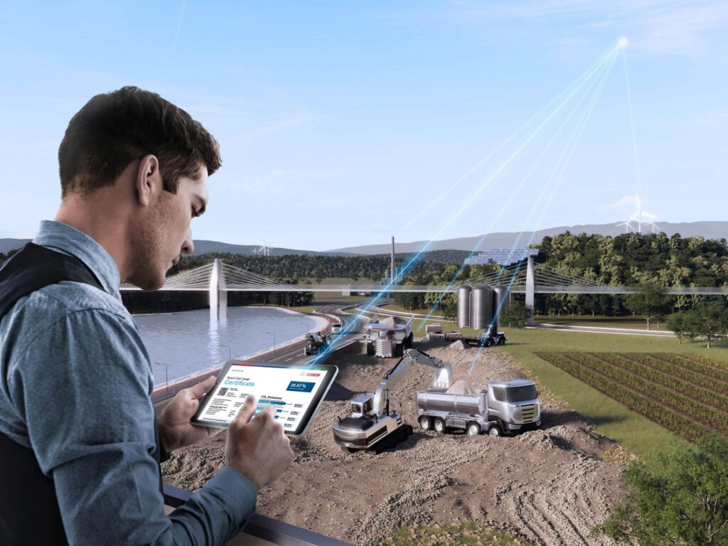 Ein Mann hält ein Tablet mit installierter Software von Bosch in der Hand, im Hintergrund Lkw und Baumaschinen