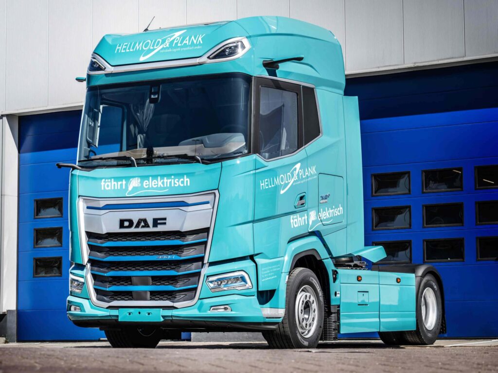 Eine batterieelektrische Sattelzugmaschine vom Typ DAF XG+ Electric in den Firmenfarben von Hellmold & Plank steht vor einem geschlossenen Hallentor