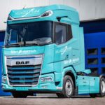 Eine batterieelektrische Sattelzugmaschine vom Typ DAF XG+ Electric in den Firmenfarben von Hellmold & Plank steht vor einem geschlossenen Hallentor