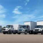 Vier mittelschwere Hauben-Lkw der Serie Freightliner M2 106 nebeneinander auf einem Parkplatz