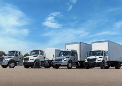 Daimler Truck North America mit Cummins-Benziner Vier mittelschwere Hauben-Lkw der Serie Freightliner M2 106 nebeneinander auf einem Parkplatz