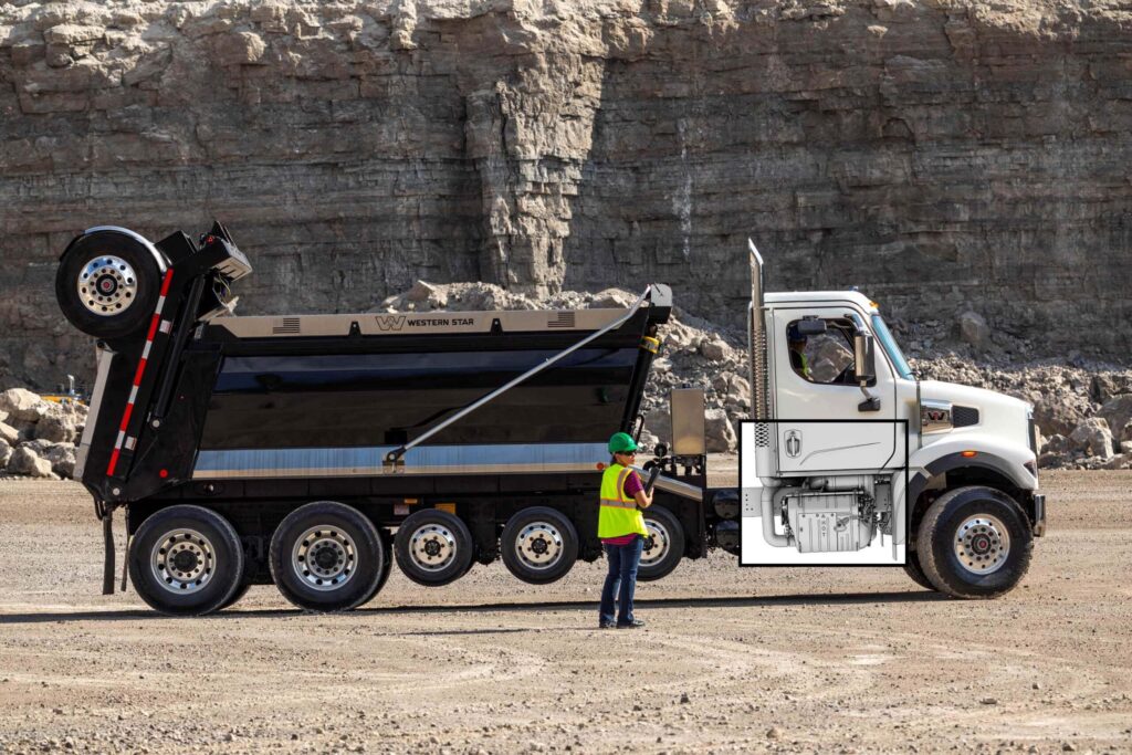 Schwerer Baustellen-Lkw der US-Marke Western Star mit überblendeter Illustration des eingebauten Motors der neuen Gen 6-Generation von Detroit Diesel; im Hintergrund eine Felswand, vor dem Lkw steht eine Arbeiterin