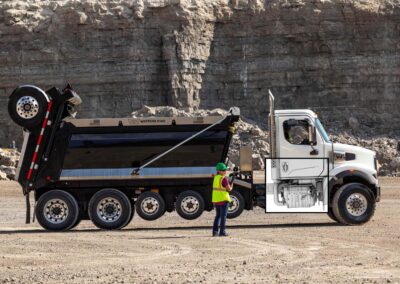 Schwerer Baustellen-Lkw der US-Marke Western Star mit überblendeter Illustration des eingebauten Motors der neuen Gen 6-Generation von Detroit Diesel; im Hintergrund eine Felswand, vor dem Lkw steht eine Arbeiterin