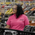 Eine Arbeiterin von Daimler Truck North America steht in der Nahaufnahme in einer Produktionshalle, umgeben von Lkw-Komponenten und Materialkisten
