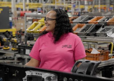 Eine Arbeiterin von Daimler Truck North America steht in der Nahaufnahme in einer Produktionshalle, umgeben von Lkw-Komponenten und Materialkisten