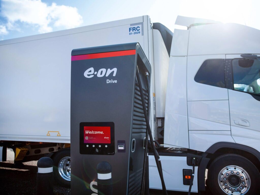 Im Vordergrund eine Ladesäule für Elektro-Lkw mit Aufschrift E.ON, im Hintergrund ein E-Lkw