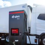 Im Vordergrund eine Ladesäule für Elektro-Lkw mit Aufschrift E.ON, im Hintergrund ein E-Lkw