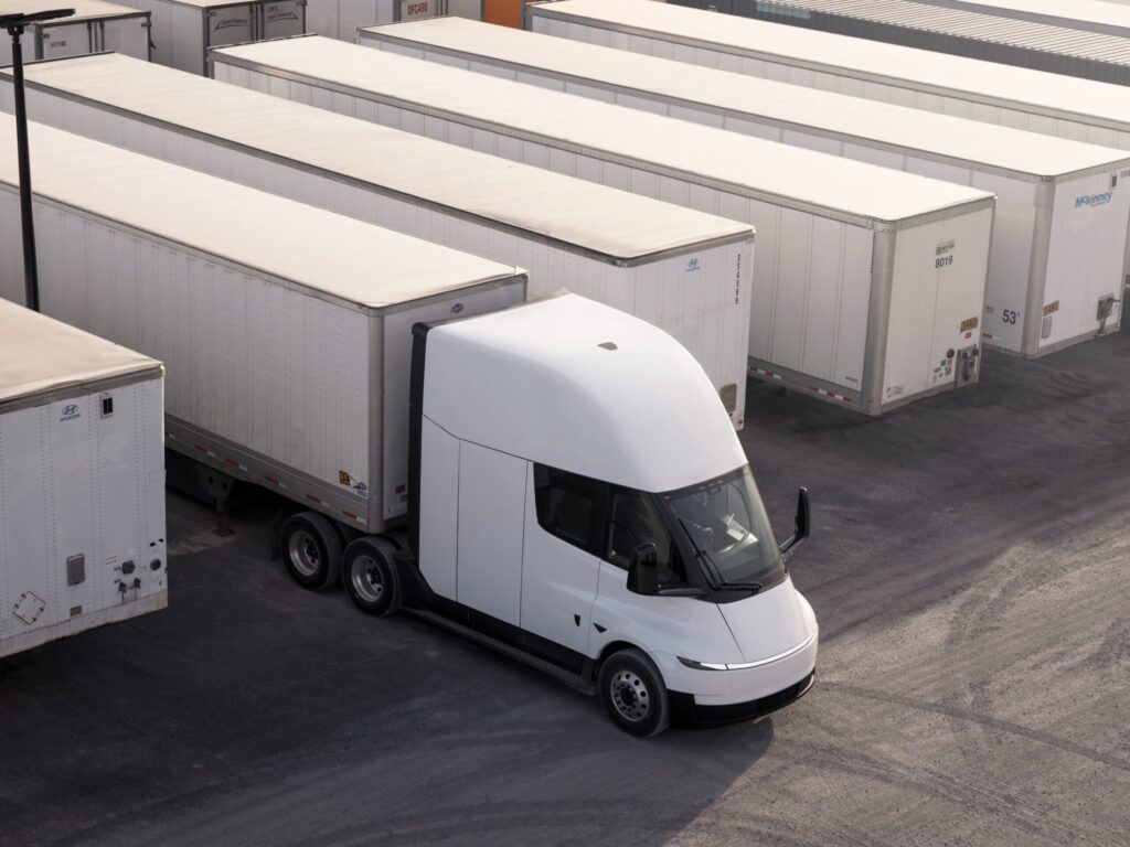 Eine batterieelektrische Sattelzugmaschine vom Typ Tesla Semi auf einem Terminalgelände mit zahlreichen abgestellten Sattelaufliegern