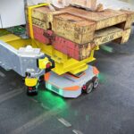 Ein Schwerlast-Schwarmfahrzeug des Karlsruher Start-ups Formic in Form eines kompakten AGV unter einer Ecke einer zu Testzwecken transportierten Ballastbrücke