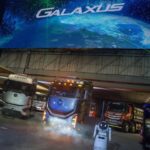 Eine große, abgedunkelte Bühne mit mehreren schweren Lkw der chinesischen Marke Foton; im Vordergrund filmen Zuschauer mit ihren Mobiltelefonen