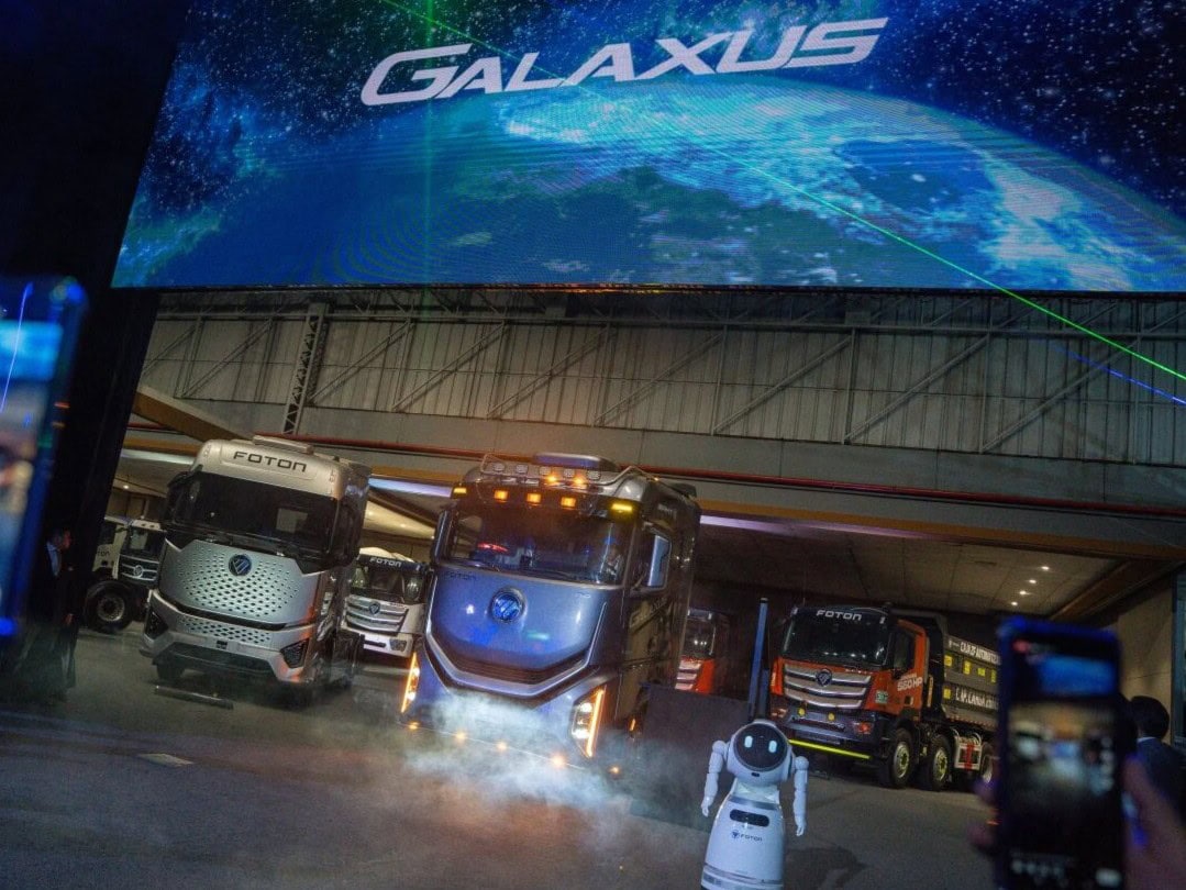 Eine große, abgedunkelte Bühne mit mehreren schweren Lkw der chinesischen Marke Foton; im Vordergrund filmen Zuschauer mit ihren Mobiltelefonen