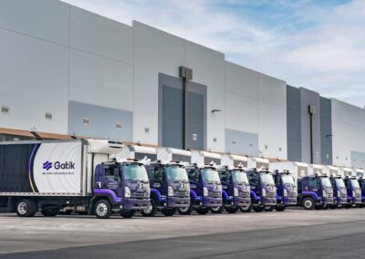 Gatik AI: Autonomer Lieferverkehr im Realbetrieb Rund ein Dutzend autonom fahrender Lkw, basierend auf der Isuzu N-Serie mit dem System „Gatik Driver“, stehen in einer Reihe vor einem Lagerhaus