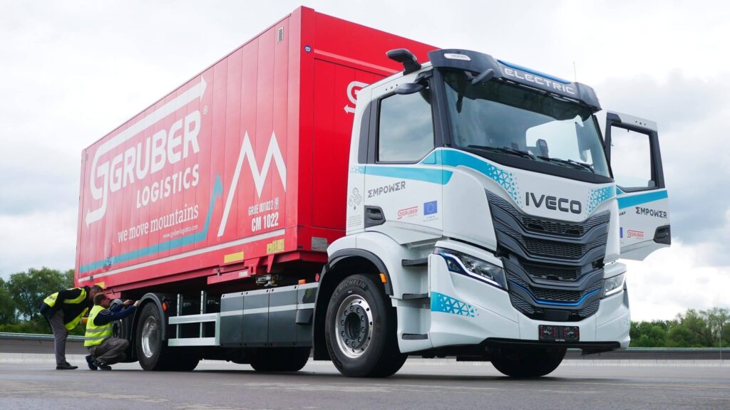 Ein dreiachsiger E-Lkw vom Typ Iveco S-eWay mit aufgebautem Wechselrahmen und Wechselbrücke von Gruber Logistics auf einem Parkplatz