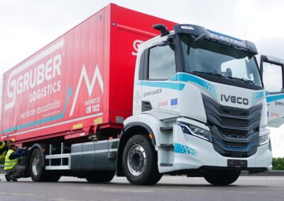 Ein dreiachsiger E-Lkw vom Typ Iveco S-eWay mit aufgebautem Wechselrahmen und Wechselbrücke von Gruber Logistics auf einem Parkplatz