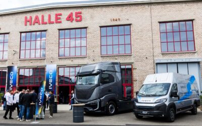 Blick auf den Veranstaltungsort „Halle 45“ in Mainz, vor der Halle stehen mehrere Menschen an Stehtischen und Fahrzeuge von Iveco (ein Transporter und eine Elektro-Sattelzugmaschine)