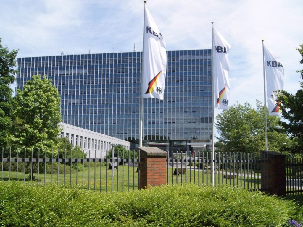 Außenansicht des KBA-Hauptgebäudes in Flensburg, davor drei wehende Fahnen mit KBA-Schriftzug