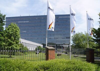 i-kfz-App jetzt auch für Unternehmen Außenansicht des KBA-Hauptgebäudes in Flensburg, davor drei wehende Fahnen mit KBA-Schriftzug