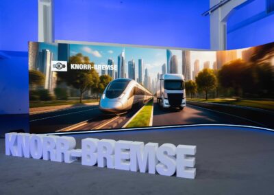 Foto einer Bühne, vorne mit dem Schriftzug von Knorr-Bremse in 3-D und hinten einer Leinwand mit Bildern eines Zugs und eines Lkw