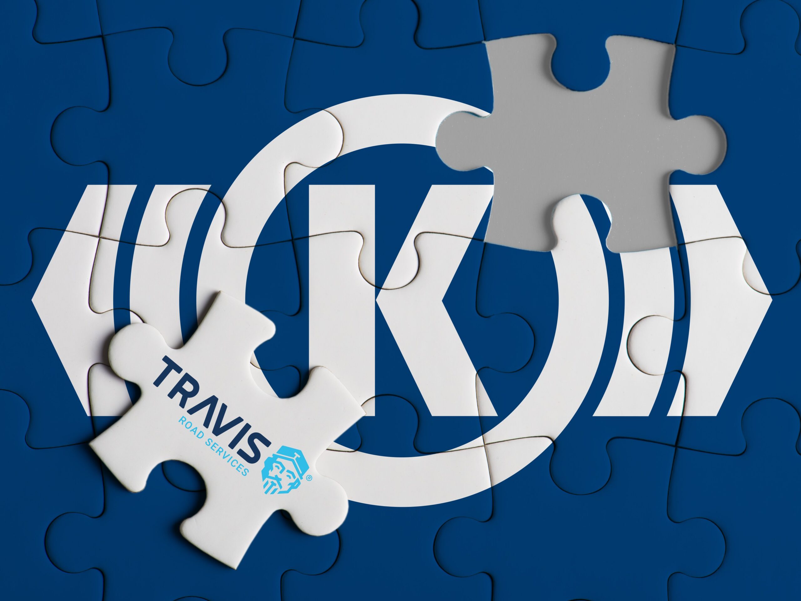 Das Logo von Knorr-Bremse auf einem kleinen Puzzle, auf dem ein neues Teil mit dem Logo von Travis liegt