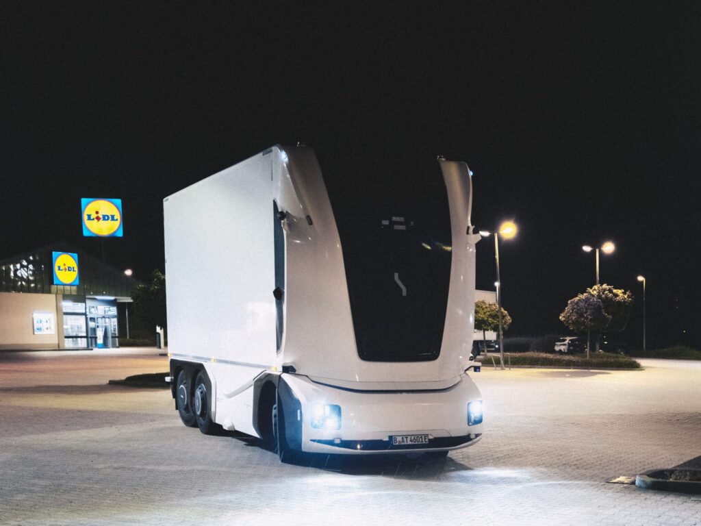 Ein kabinenloser E-Lkw, den Lidl und Einride in einem Projekt auf öffentlichen Straßen einsetzen. Das dreiachsige Fahrzeug mit Kofferaufbau steht bei Nacht vor einer Lidl-Filiale