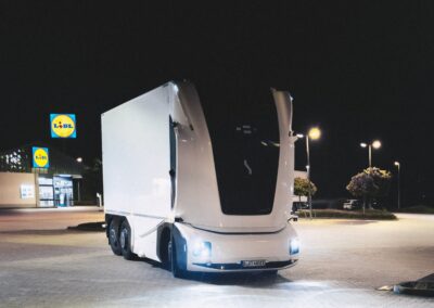 Lidl und Einride bringen autonomen E-Lkw auf öffentliche Straßen Ein kabinenloser E-Lkw, den Lidl und Einride in einem Projekt auf öffentlichen Straßen einsetzen. Das dreiachsige Fahrzeug mit Kofferaufbau steht bei Nacht vor einer Lidl-Filiale