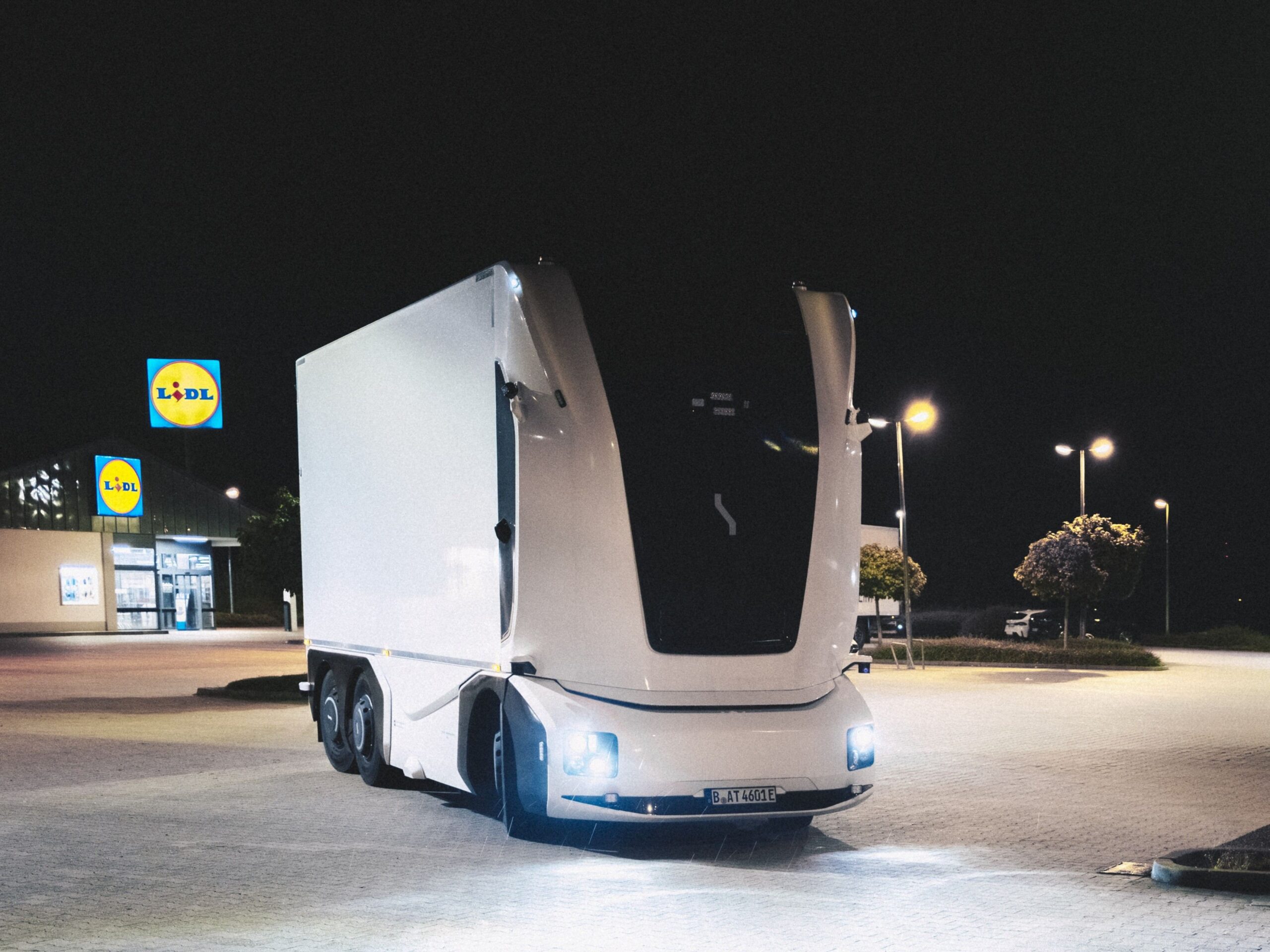 Ein kabinenloser E-Lkw, den Lidl und Einride in einem Projekt auf öffentlichen Straßen einsetzen. Das dreiachsige Fahrzeug mit Kofferaufbau steht bei Nacht vor einer Lidl-Filiale