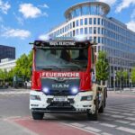 Der erste batterieelektrische MAN eTGS für die Feuerwehr, ein Dreiachser als Wechsellader mit Aufbau von Meiller vor städtischer Kulisse