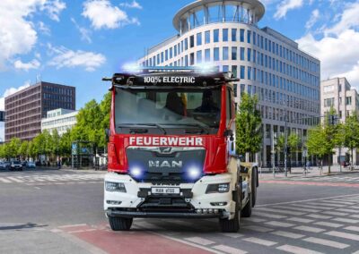 Erster vollelektrischer MAN eTGS für die Feuerwehr Der erste batterieelektrische MAN eTGS für die Feuerwehr, ein Dreiachser als Wechsellader mit Aufbau von Meiller vor städtischer Kulisse