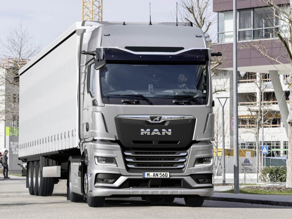 Ein Sattelzug mit einem MAN TGX auf einer innerstädtischen Straße; die Sattelzugmaschine ist mit dem System Optiview Basic ausgestattet, eine Kombination aus Kameras statt der Rückspiegel und einem konventionellen Frontspiegel