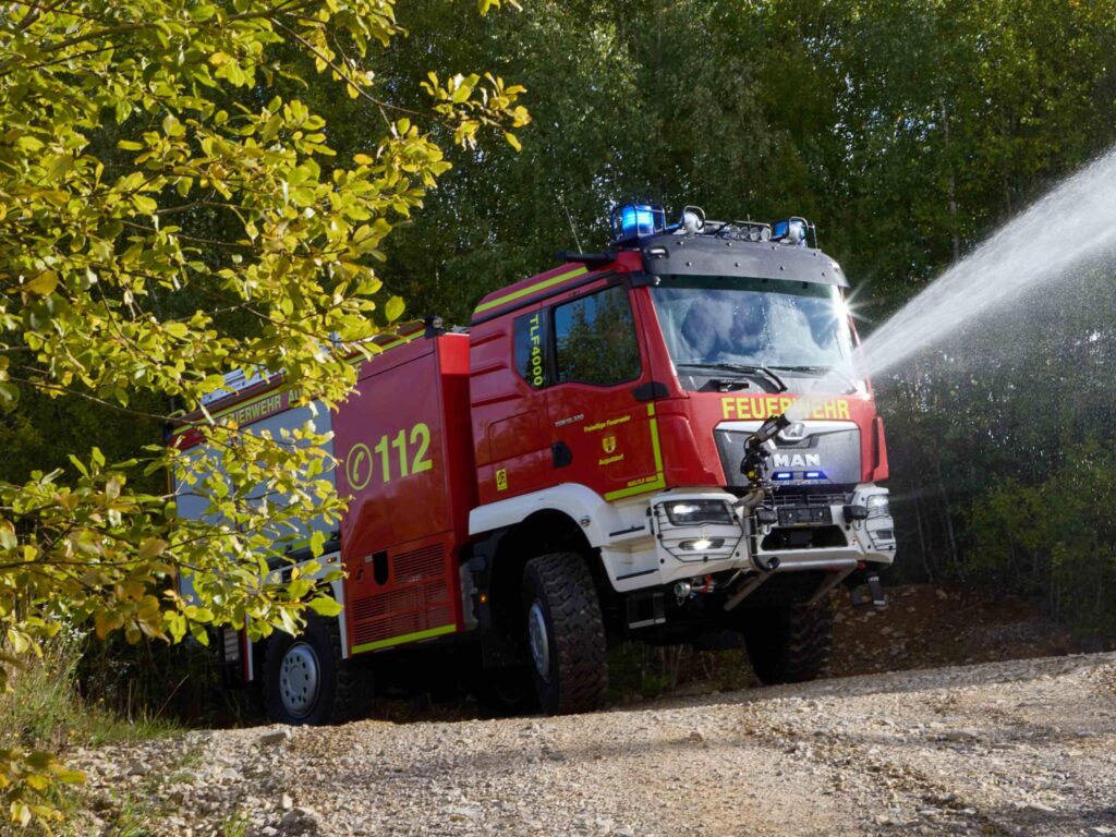 Ein Feuerwehrfahrzeug auf Basis eines MAN TGM 18.320 4x4 befährt einen Waldweg und spritzt dabei zu Demonstrationszwecken Löschwasser in die Böschung