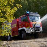 Ein Feuerwehrfahrzeug auf Basis eines MAN TGM 18.320 4x4 befährt einen Waldweg und spritzt dabei zu Demonstrationszwecken Löschwasser in die Böschung