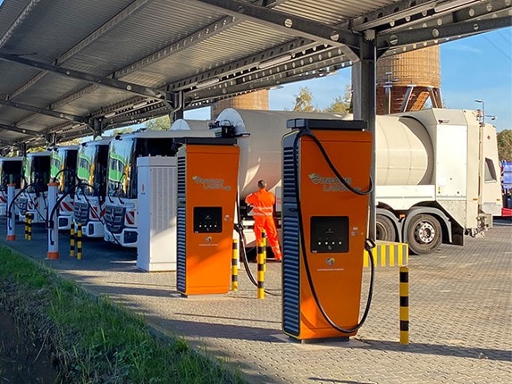 Mehrere Müllsammelfahrzeuge auf Basis batterieelektrischer Lkw stehen in einer Reihe an einer Depot-Ladestation
