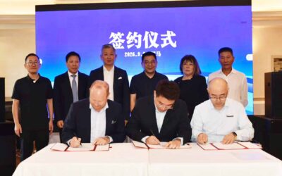 v.l.n.r: Andreas Haller (CEO Haller Group und Quantron-Gründer), Haohua Yu (CEO der Riyue Group), und Dr. Feilong Liu (CEO HyperView) unterzeichnen nebeneinandersitzend Dokumente. Im Hintergrund stehen weitere sechs Personen