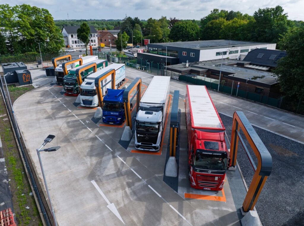 Bild eines Milence-Ladeparks für E-Lkw von schräg oben, die Ladebuchten mit sechs Lkw nebeneinander gefüllt