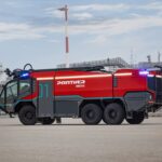 Flughafenlöschfahrzeug vom Typ Rosenbauer Panther Electric vor einem schemenhaft dargestellten Flughafen