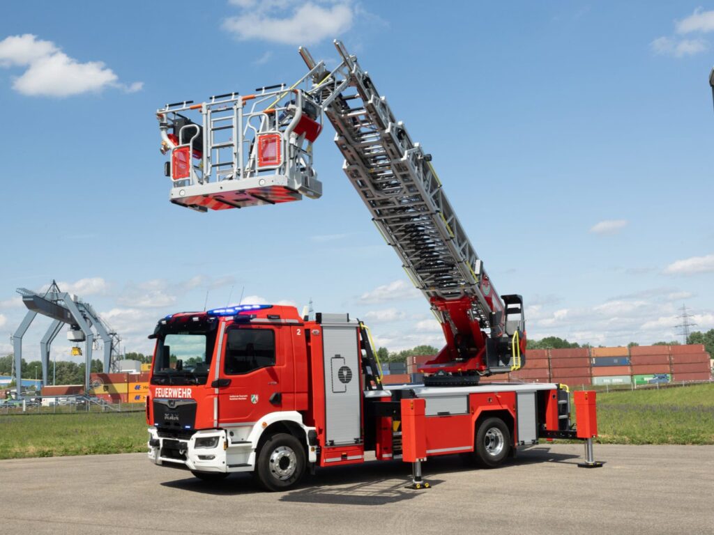 Drehleiterfahrzeug für die Feuerwehr auf einer Stellfläche, Stützen und Rettungskorb sind ausgefahren; es ist ein vollelektrisches Fahrzeug mit Aufbau von Rosenbauer auf einem MAN eTGM