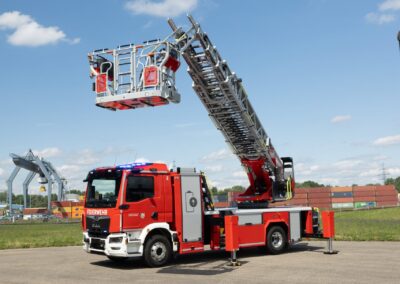Rosenbauer präsentiert vollelektrische Drehleiter Drehleiterfahrzeug für die Feuerwehr auf einer Stellfläche, Stützen und Rettungskorb sind ausgefahren; es ist ein vollelektrisches Fahrzeug mit Aufbau von Rosenbauer auf einem MAN eTGM