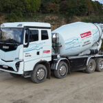 Ein batterieelektrischer E-Lkw von Sany als 8x4 mit Betonmischer-Aufbau von Putzmeister, fotografiert von schräg vorne auf sandigem Boden