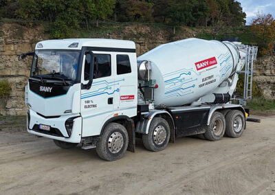 Sany stellt auf der IAA neue E-Lkw für Europa vor Ein batterieelektrischer E-Lkw von Sany als 8x4 mit Betonmischer-Aufbau von Putzmeister, fotografiert von schräg vorne auf sandigem Boden