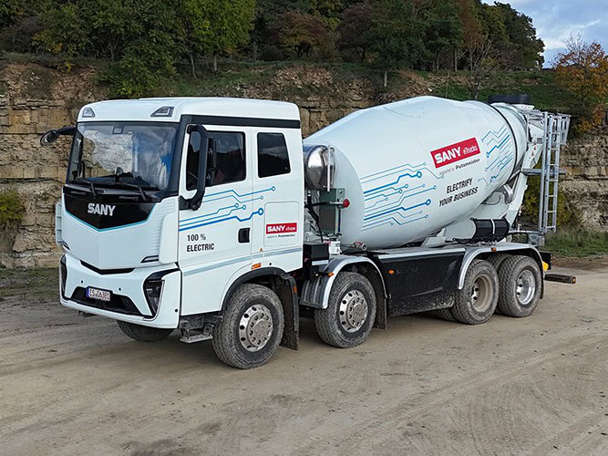 Ein batterieelektrischer E-Lkw von Sany als 8x4 mit Betonmischer-Aufbau von Putzmeister, fotografiert von schräg vorne auf sandigem Boden
